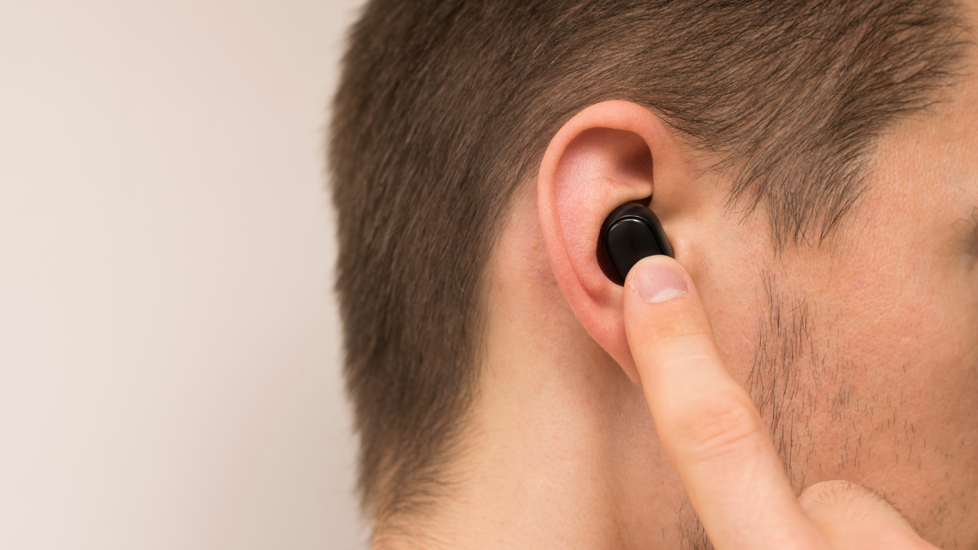 Un homme avec un écouteur sans fil dans l'oreille. L'homme allume l'écouteur sans fil avec son doigt.